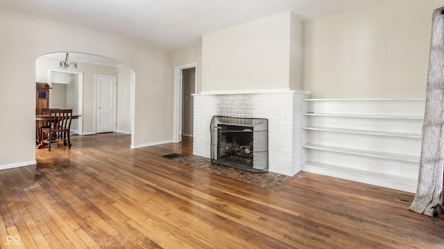 unfurnished living room featuring dark hardwood / wood-style flooring, a chandelier, and a brick fireplace