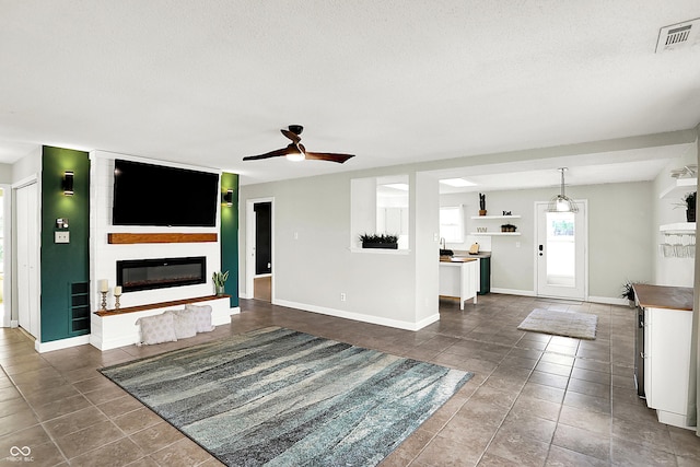 unfurnished living room with visible vents, a ceiling fan, a large fireplace, a textured ceiling, and dark tile patterned flooring