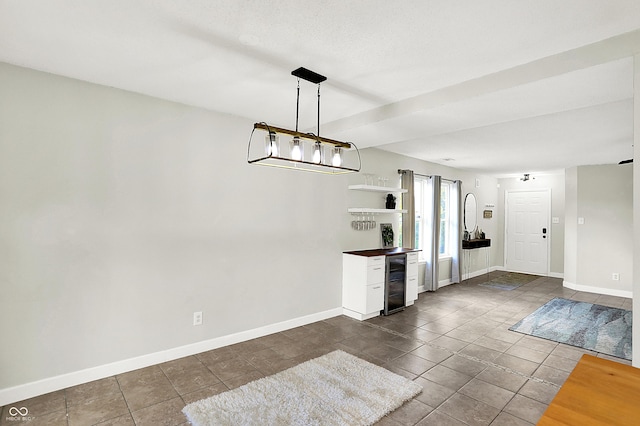 unfurnished dining area with wine cooler, dark tile patterned floors, and baseboards