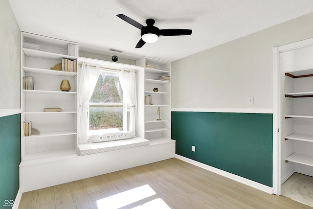 interior space with a ceiling fan, a textured ceiling, baseboards, and wood finished floors