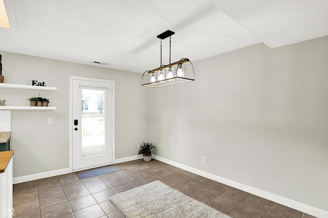 unfurnished dining area with visible vents, baseboards, a textured ceiling, and dark tile patterned flooring