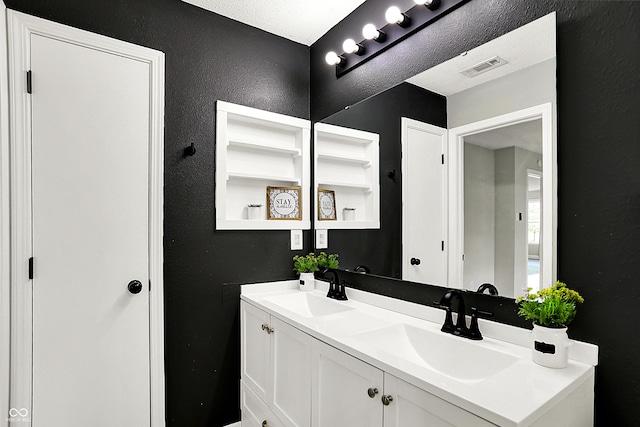 bathroom with double vanity, visible vents, a sink, and a textured wall