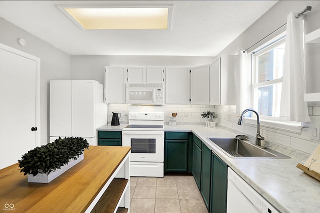 kitchen featuring light tile patterned floors, tasteful backsplash, green cabinets, a sink, and white appliances