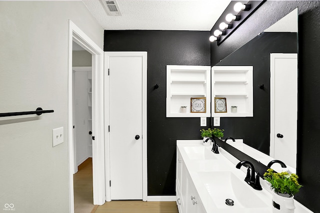 bathroom featuring visible vents, a sink, a textured ceiling, and wood finished floors