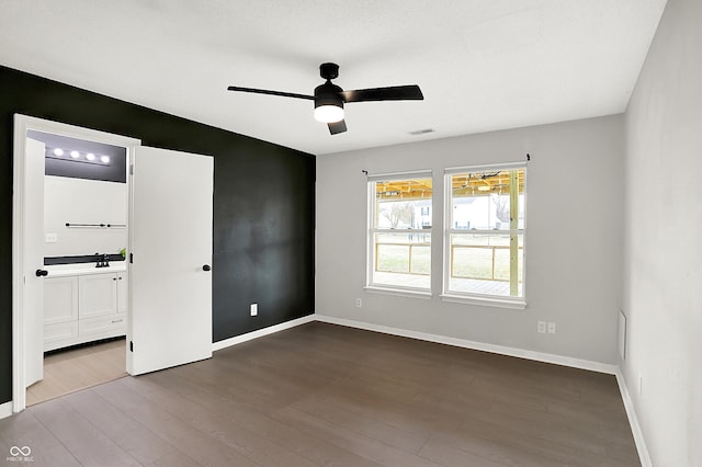 empty room featuring dark wood-style floors, visible vents, ceiling fan, and baseboards