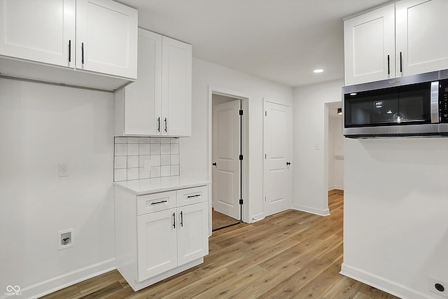 kitchen with light wood finished floors, baseboards, white cabinets, and stainless steel microwave