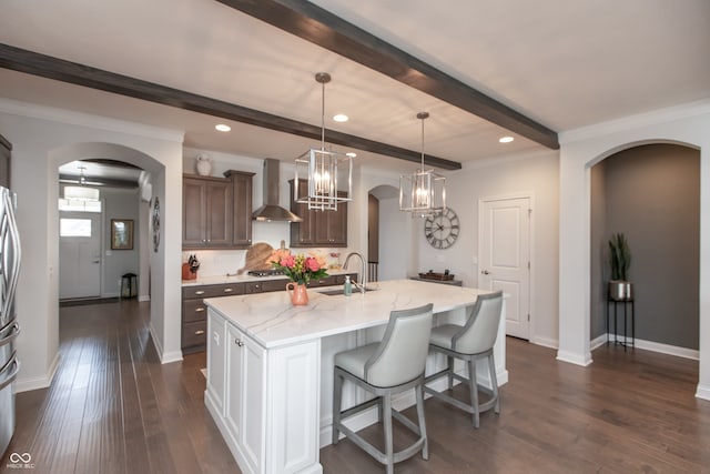 kitchen with dark wood finished floors, beam ceiling, arched walkways, stainless steel appliances, and wall chimney exhaust hood