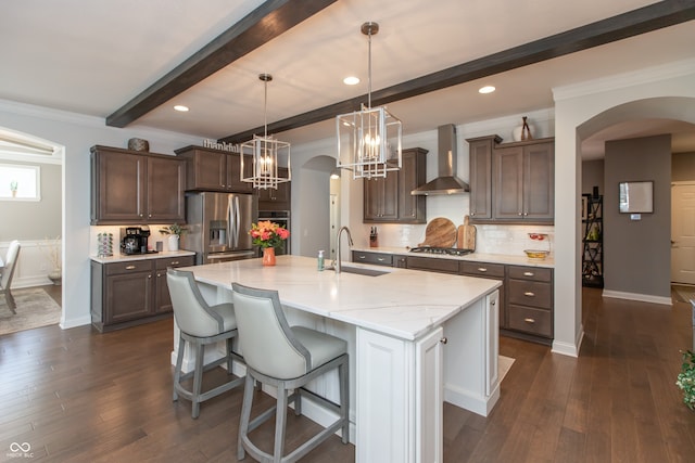 kitchen featuring a sink, tasteful backsplash, arched walkways, appliances with stainless steel finishes, and wall chimney exhaust hood