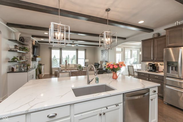 kitchen with open floor plan, a center island with sink, beamed ceiling, stainless steel appliances, and a sink