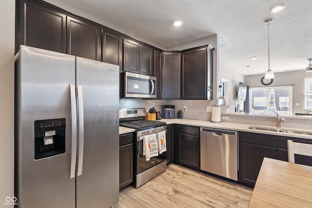 kitchen featuring appliances with stainless steel finishes, decorative light fixtures, light countertops, dark brown cabinets, and a sink