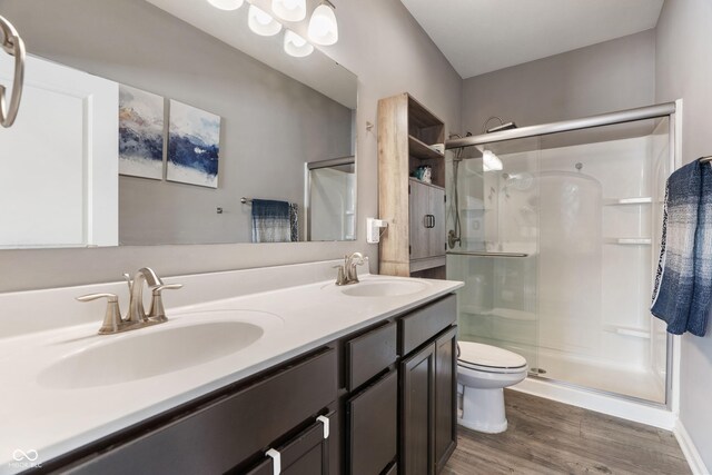 bathroom featuring double vanity, a stall shower, toilet, wood finished floors, and a sink