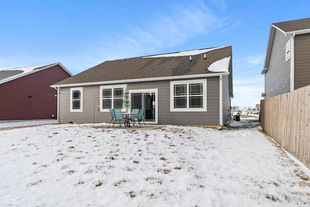 snow covered rear of property with roof with shingles and fence