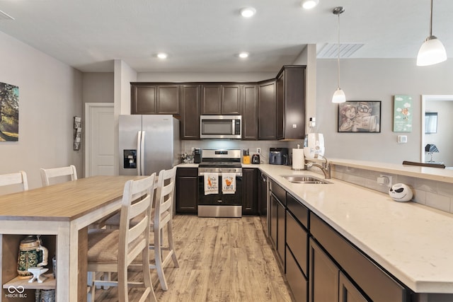 kitchen with stainless steel appliances, hanging light fixtures, backsplash, a sink, and light wood-type flooring