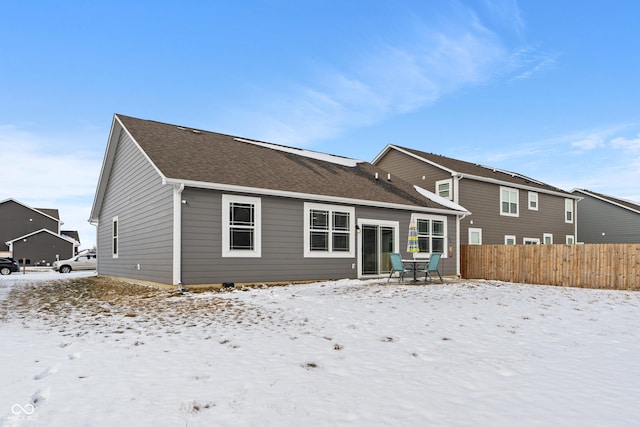 snow covered property featuring roof with shingles and fence