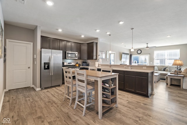 kitchen with dark brown cabinetry, appliances with stainless steel finishes, open floor plan, light countertops, and pendant lighting