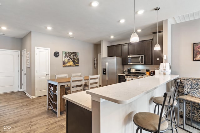 kitchen featuring visible vents, a peninsula, stainless steel appliances, light wood-style floors, and pendant lighting