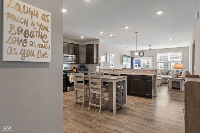 kitchen featuring dark brown cabinetry, open floor plan, light countertops, appliances with stainless steel finishes, and a center island