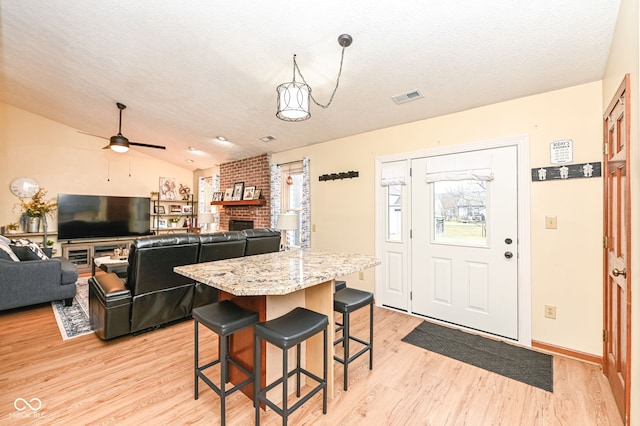 kitchen with light hardwood / wood-style flooring, light stone countertops, a textured ceiling, a breakfast bar, and a center island