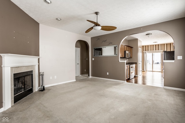 unfurnished living room featuring baseboards, a tile fireplace, a textured ceiling, ceiling fan, and light carpet