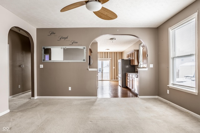 empty room with plenty of natural light, arched walkways, a textured ceiling, and carpet