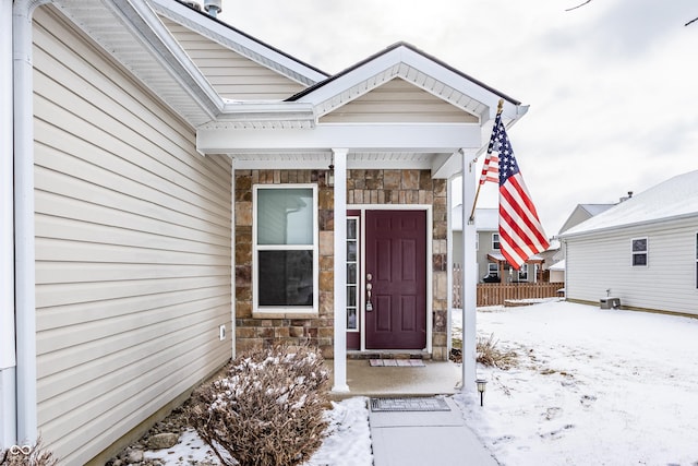 snow covered property entrance with stone siding