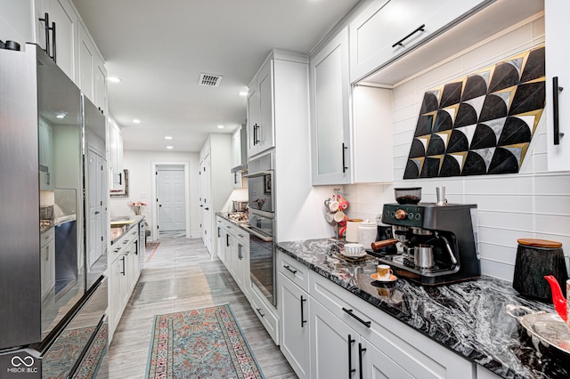 kitchen with recessed lighting, stainless steel appliances, backsplash, light wood finished floors, and dark stone countertops