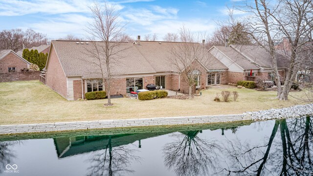 back of property with a water view, a yard, a patio, and brick siding