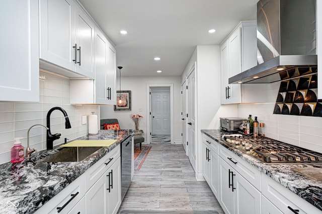 kitchen featuring wall chimney exhaust hood, dark stone countertops, a sink, and stainless steel appliances