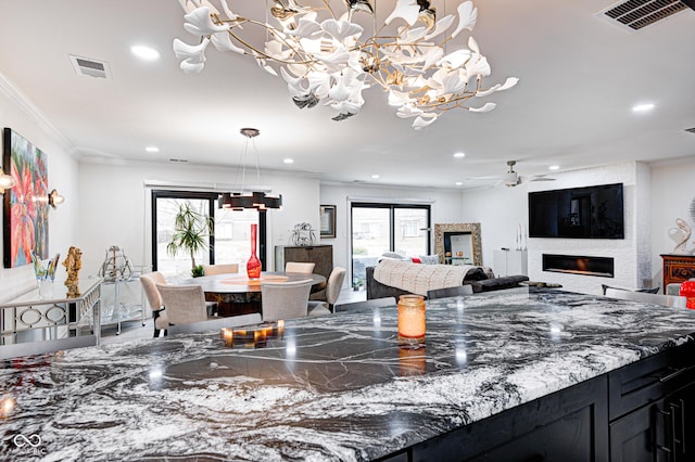 dining area with a fireplace, visible vents, crown molding, and ceiling fan with notable chandelier