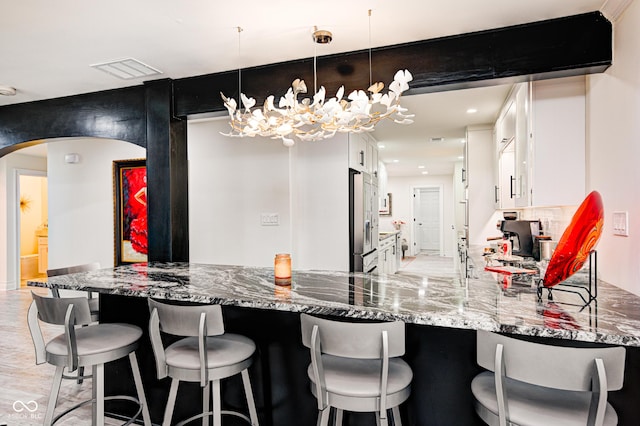 bar featuring visible vents, arched walkways, stainless steel fridge with ice dispenser, decorative light fixtures, and backsplash