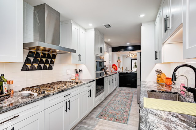 kitchen with visible vents, light stone counters, stainless steel appliances, wall chimney range hood, and a sink