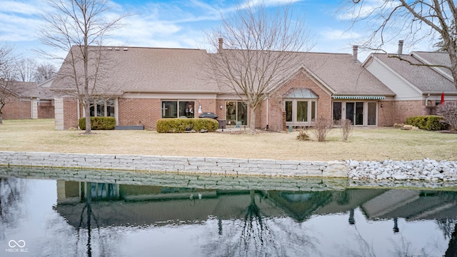 back of property featuring a yard, brick siding, a water view, and a shingled roof