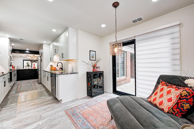 kitchen with a sink, white cabinetry, visible vents, light wood-style floors, and backsplash