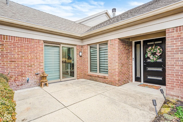 entrance to property with roof with shingles, a patio, and brick siding