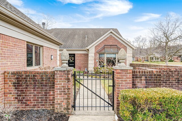 view of front of house with roof with shingles, brick siding, a fenced front yard, and a gate