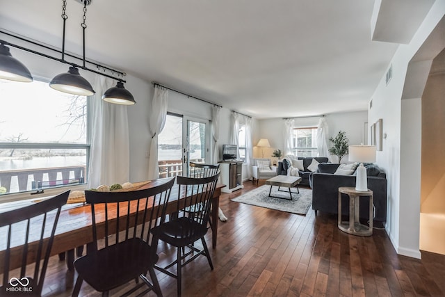 dining space with dark wood-type flooring, french doors, a water view, and a wealth of natural light