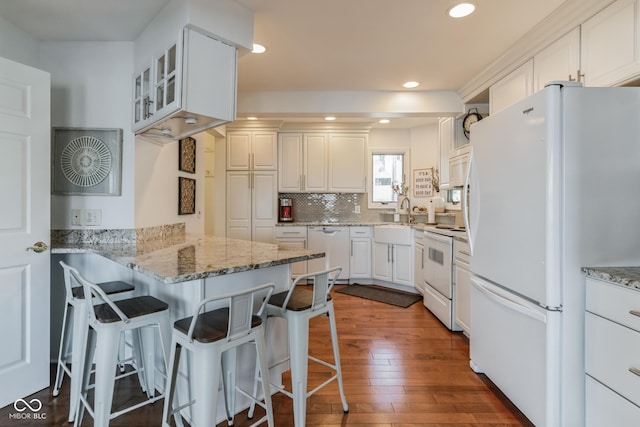 kitchen featuring white cabinets, kitchen peninsula, a breakfast bar area, and white appliances