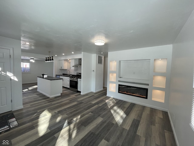 kitchen featuring white cabinets, a glass covered fireplace, dark countertops, hanging light fixtures, and stainless steel gas range