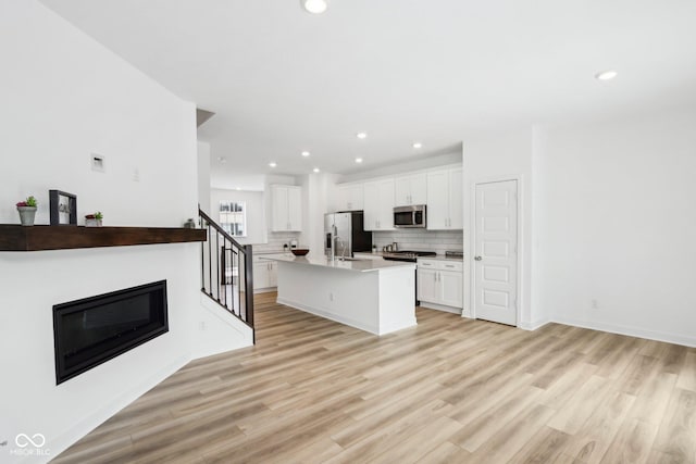 kitchen featuring white cabinetry, a center island with sink, stainless steel appliances, and light hardwood / wood-style flooring