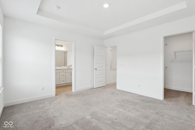 unfurnished bedroom featuring a closet, connected bathroom, a raised ceiling, a walk in closet, and light colored carpet