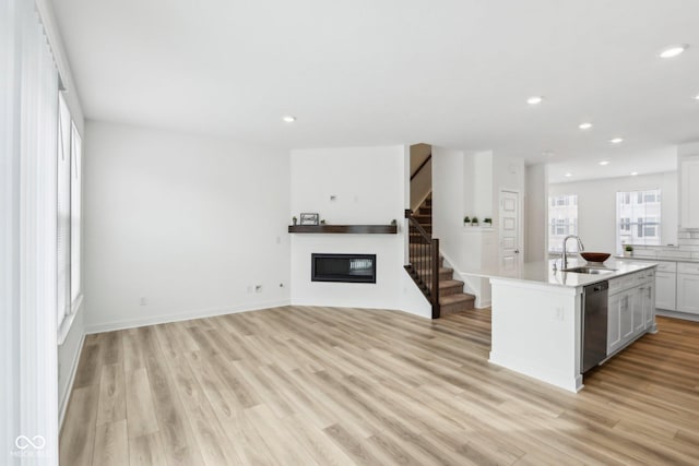 kitchen with sink, white cabinetry, dishwasher, light hardwood / wood-style floors, and an island with sink