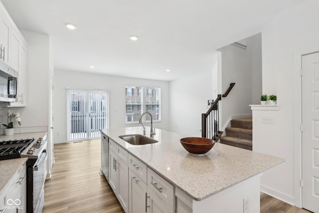 kitchen with sink, appliances with stainless steel finishes, a kitchen island with sink, and white cabinetry