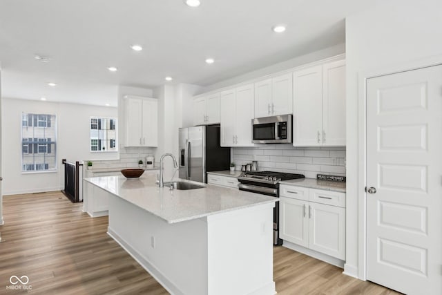 kitchen with appliances with stainless steel finishes, sink, white cabinets, and a center island with sink