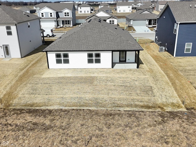 back of property with a yard, cooling unit, a residential view, and roof with shingles