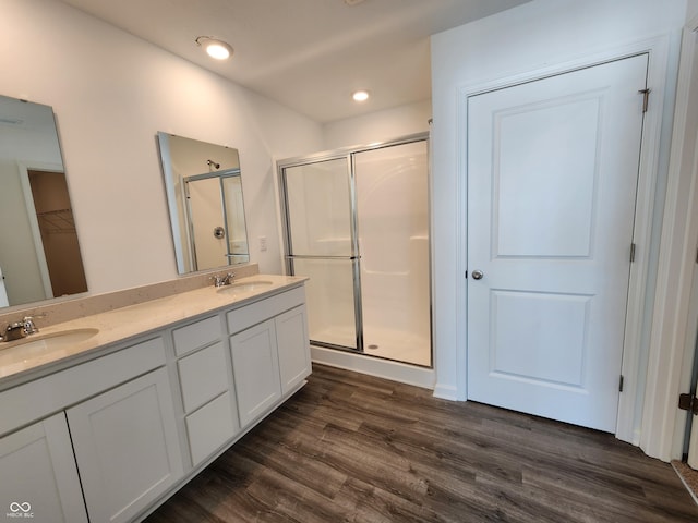 full bath with a stall shower, wood finished floors, double vanity, and a sink