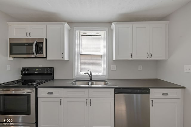 kitchen featuring dark countertops, white cabinets, appliances with stainless steel finishes, and a sink