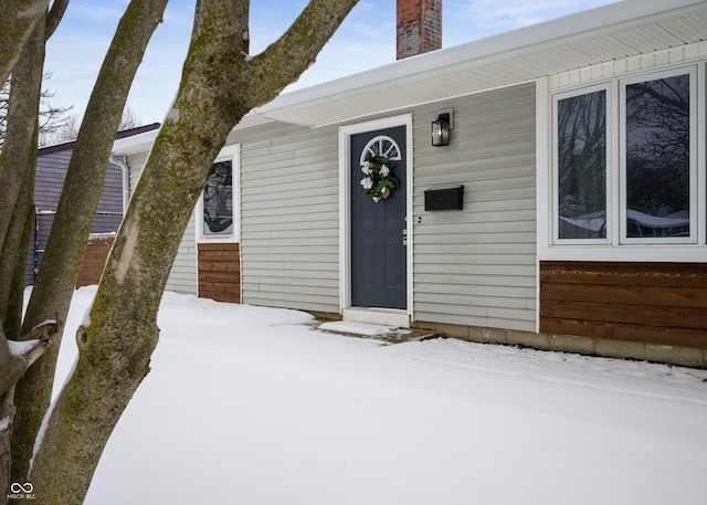 snow covered property entrance featuring a chimney