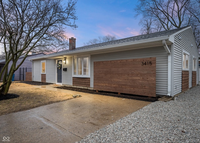 ranch-style home featuring a shingled roof, gravel driveway, a chimney, and an attached garage