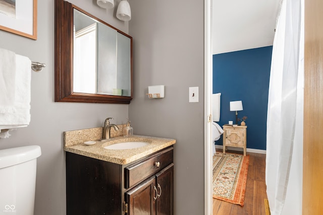 bathroom featuring toilet, connected bathroom, vanity, wood finished floors, and baseboards