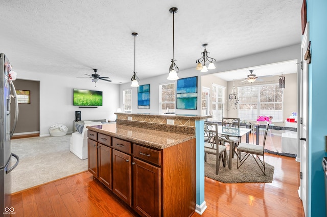 kitchen featuring wood-type flooring, a textured ceiling, dark stone counters, pendant lighting, and stainless steel refrigerator